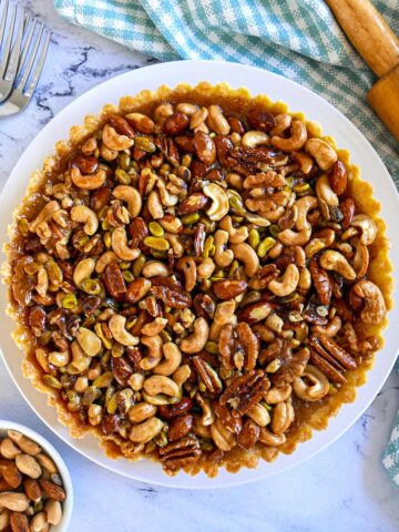 caramel nut tart on a white platter with rolling pin in the background