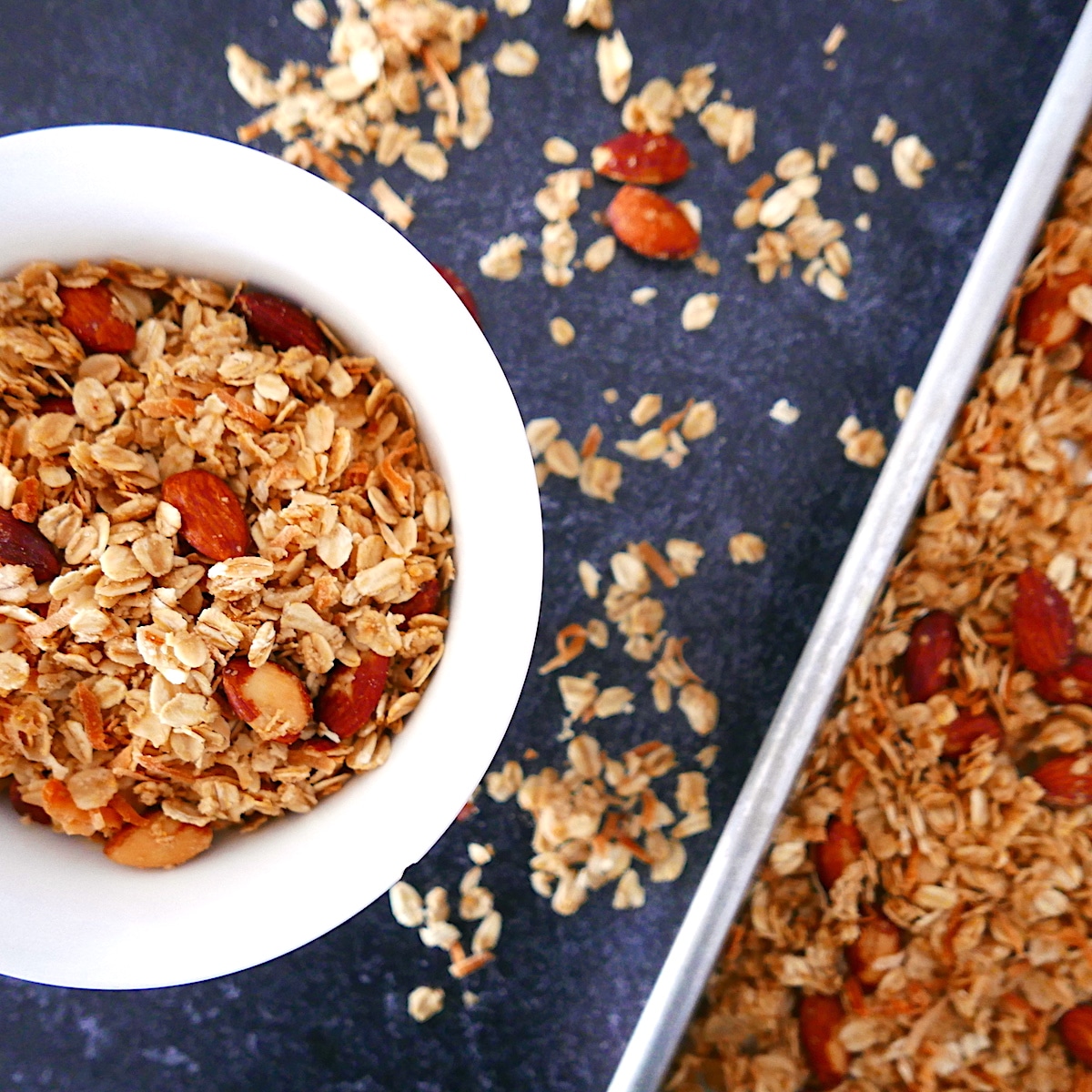 White bowl of granola with pan of granola next to it.