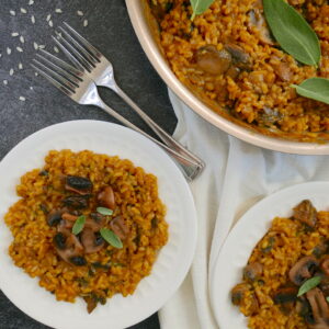 pumpkin and mushroom risotto on two white plates with pan in background and two forks