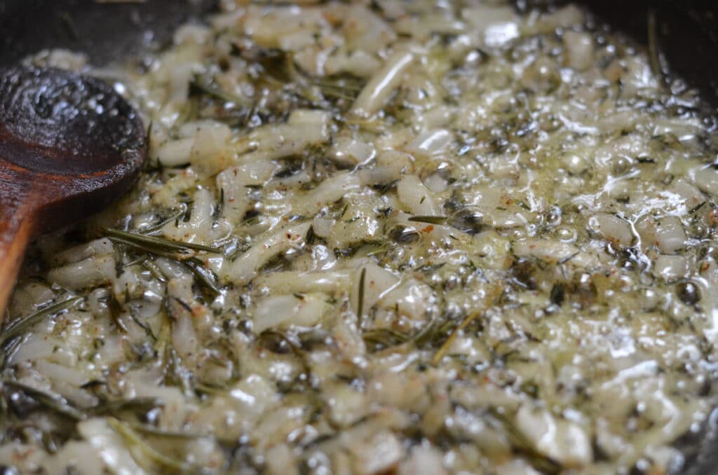 onions being sauteed with thyme and garlic in a pan