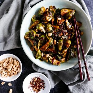 asian brussels sprouts in a white bowl with chopsticks next to a gray napkin