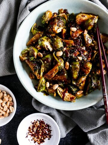 asian brussels sprouts in a white bowl with chopsticks next to a gray napkin
