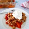 peach crisp with brown butter crumble on a white plate with a spoon and whipped cream.