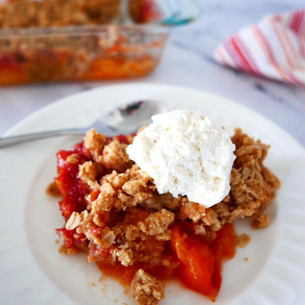 peach crisp with brown butter crumble on a plate with a spoon and whipped cream.
