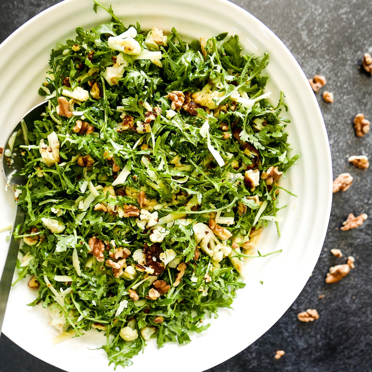 roasted cauliflower salad in a large white bowl with toasted walnuts on the table.