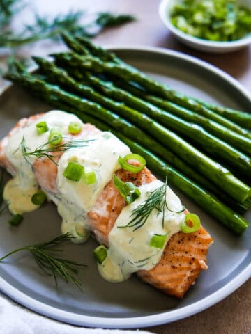 salmon with creamy mustard dill sauce on a plate with roasted asparagus.