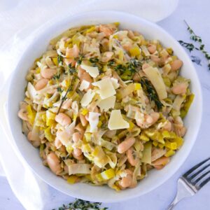 creamy braised white beans and leeks in a white bowl with white napkin