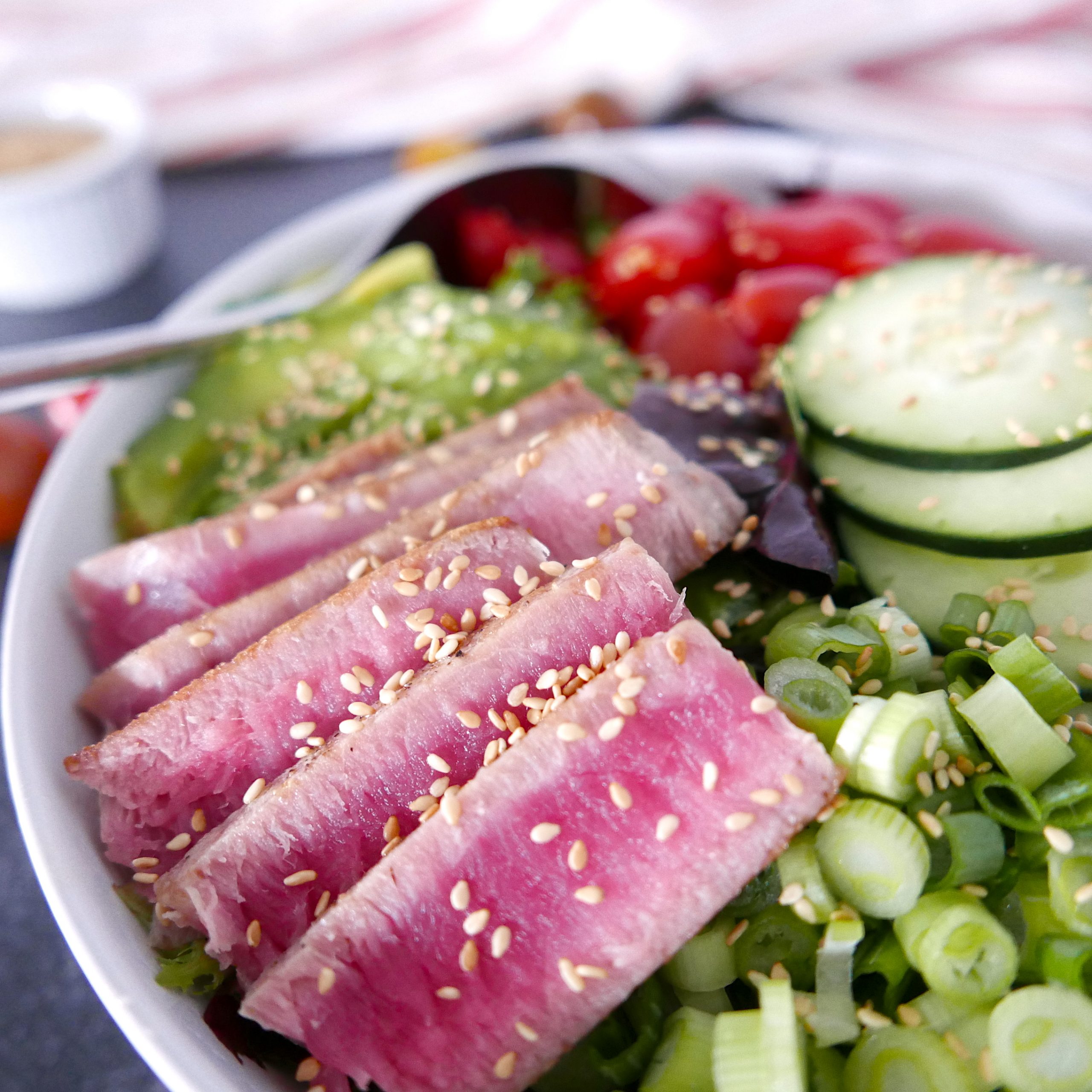 tuna steak salad in a white bowl with cucumbers, scallions, avocado, and cherry tomatoes.