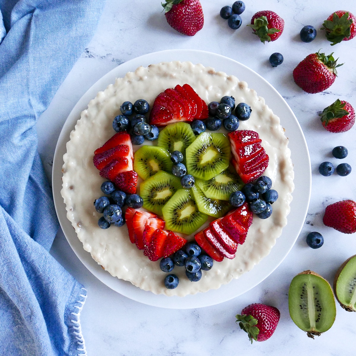 vegan-fruit-tart-on-a-white-platter.jpg vegan fruit tart with kiwi and berries on a platter and surrounded by more berries.