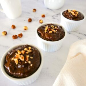 three cups of chocolate avocado pudding topped with chopped hazelnuts