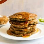 Syrup being poured on stack of pancakes.