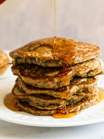 Syrup being poured on stack of pancakes.