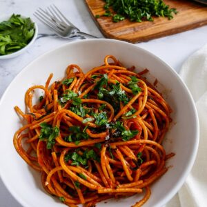 caramelized shallot pasta with greens in a white bowl garnished with parsley and cutting board in background with chopped parsley