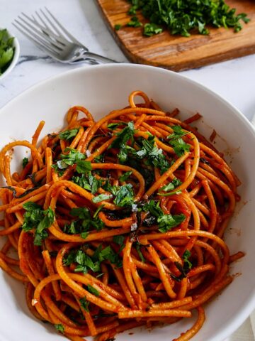 caramelized shallot pasta with greens in a white bowl garnished with parsley and cutting board in background with chopped parsley