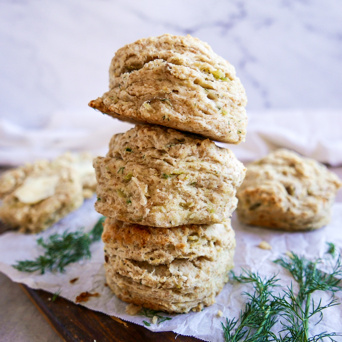 stack of three potato biscuits on a cutting board with fresh dill next to them.
