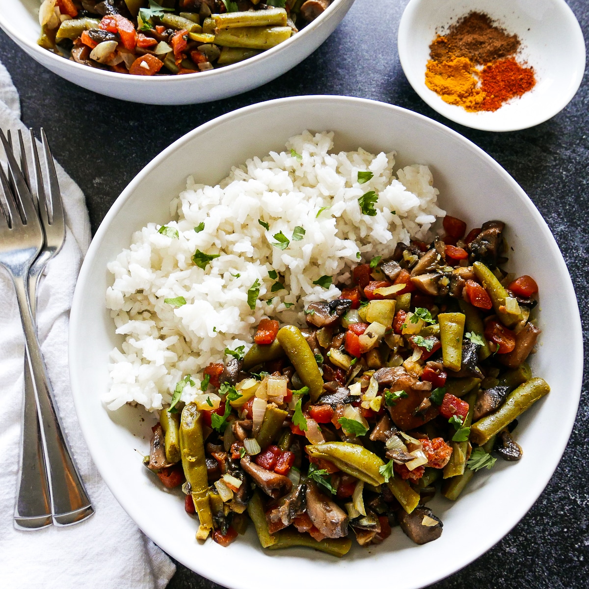 Bowl of green bean curry with white rice and two forks.