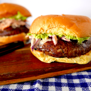 two portobello burgers sitting on a wooden cheese board