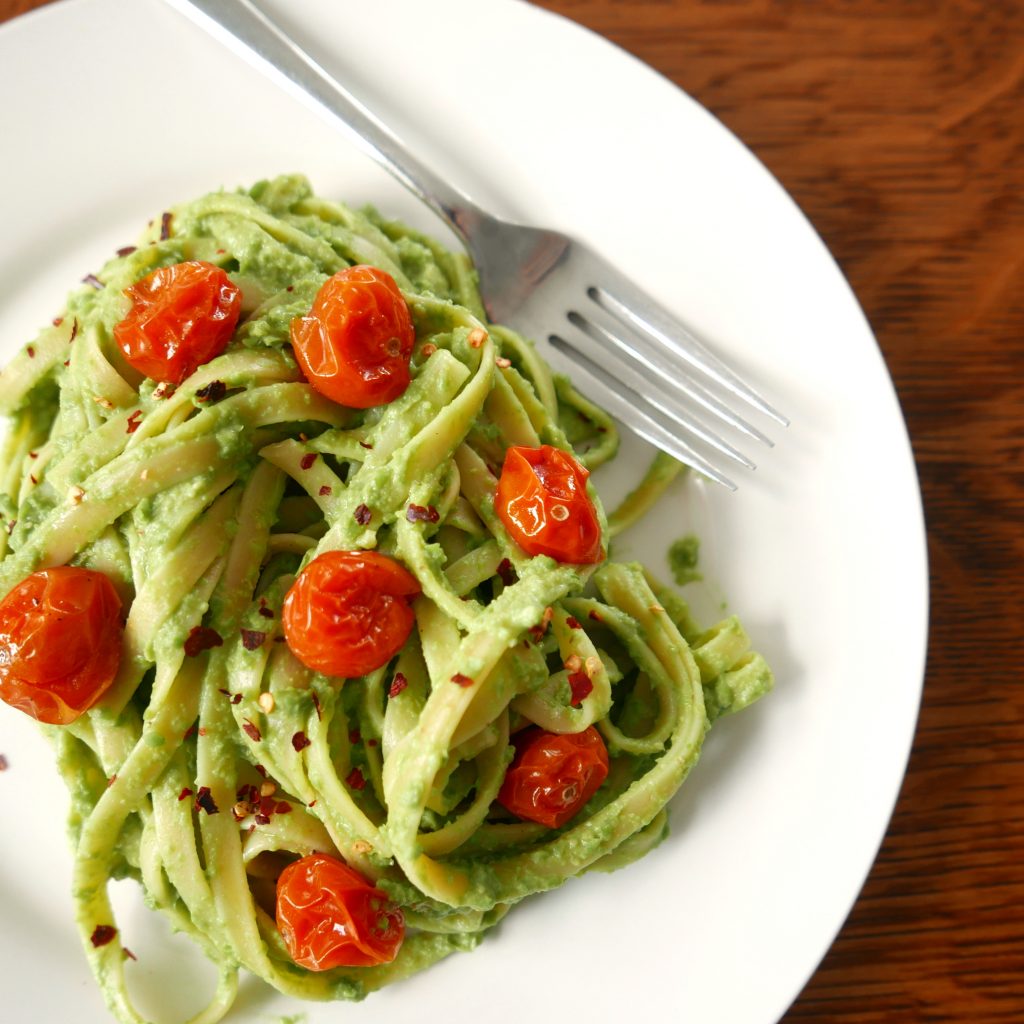fettuccine with red roasted tomatoes on a white plate with a silver fork sitting on a wooden table