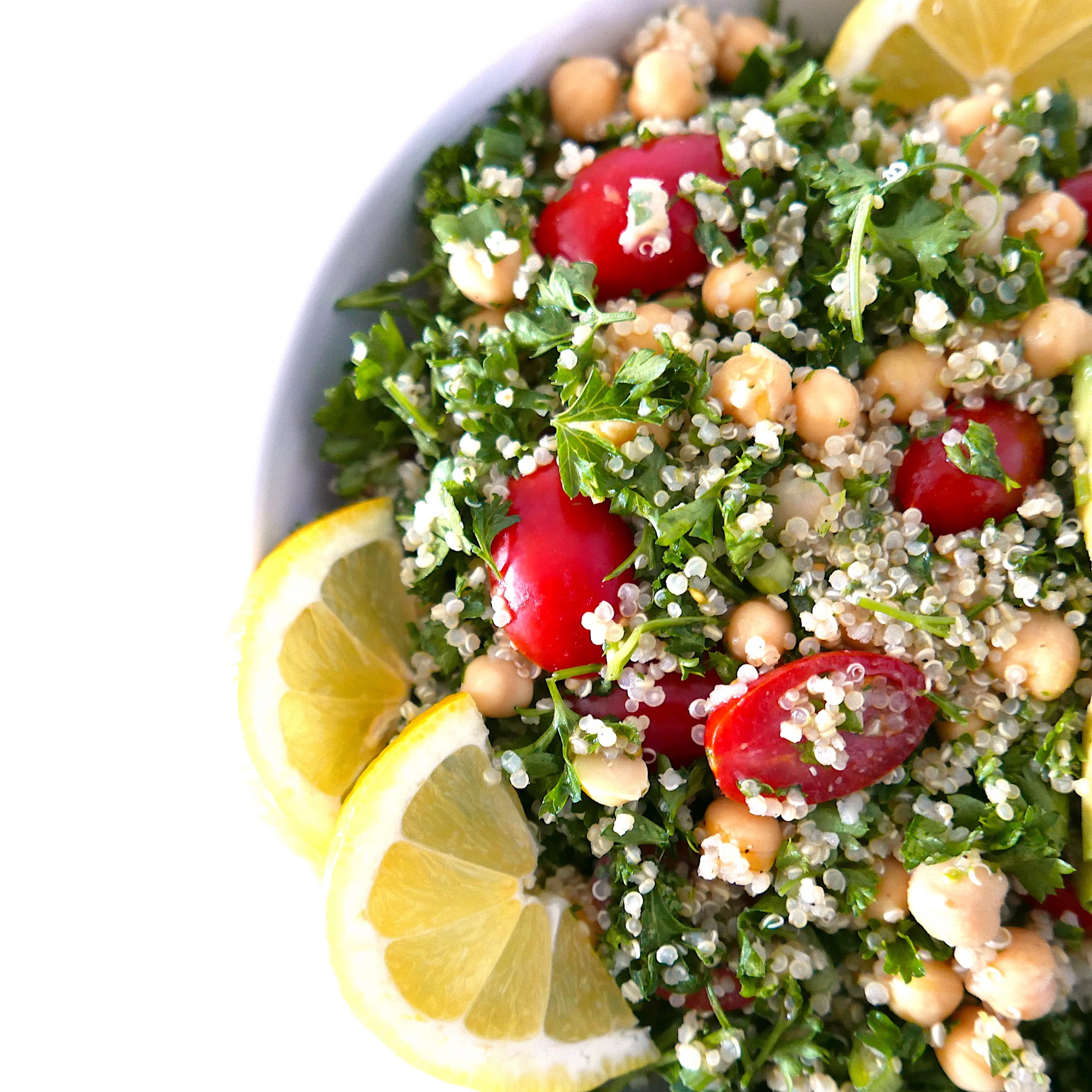 tabbouleh salad in a white bowl with lemon wedges arranged on top.