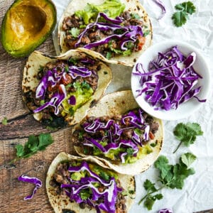 refried bean and cheese tacos arranged on a table with avocaco and cabbage.