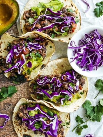 refried bean and cheese tacos arranged on a table with avocaco and cabbage.