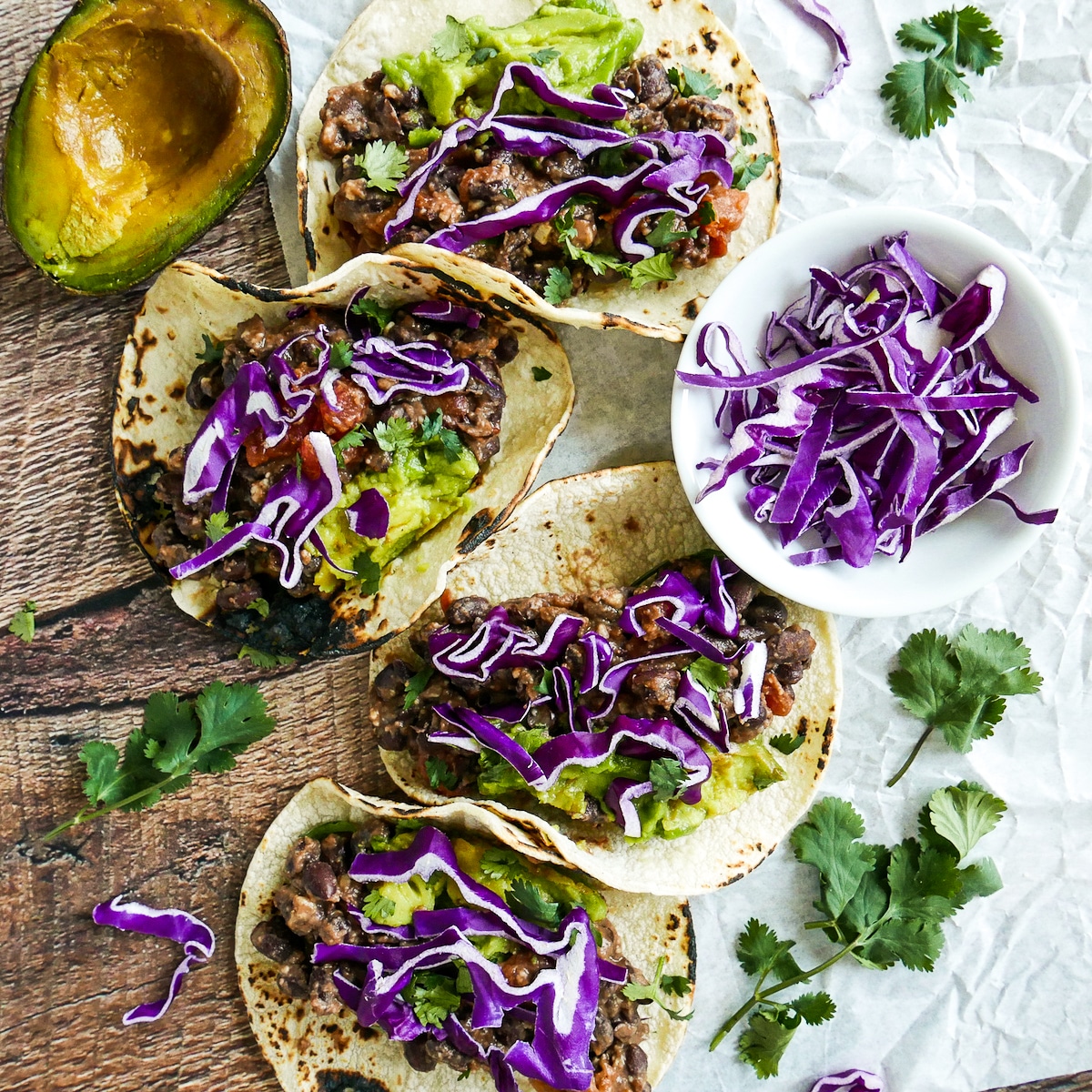 Refried bean tacos arranged on a table with avocaco and cabbage.