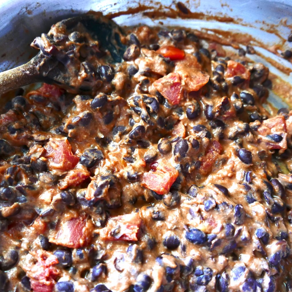 refried black bean and cheese filling for tacos in a silver frying pan