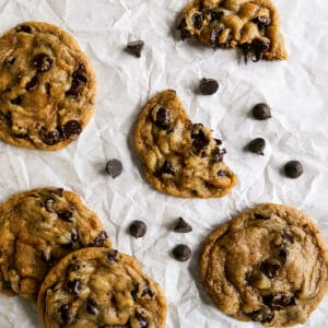 five brown butter chocolate chip cookies arranged on parchment paper with chocolate chips.