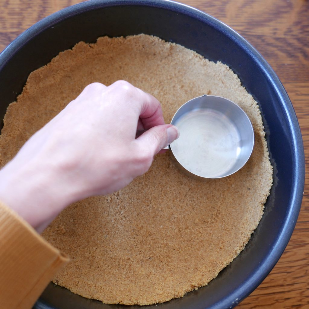 a white hand setting graham cracker crust into pie shell