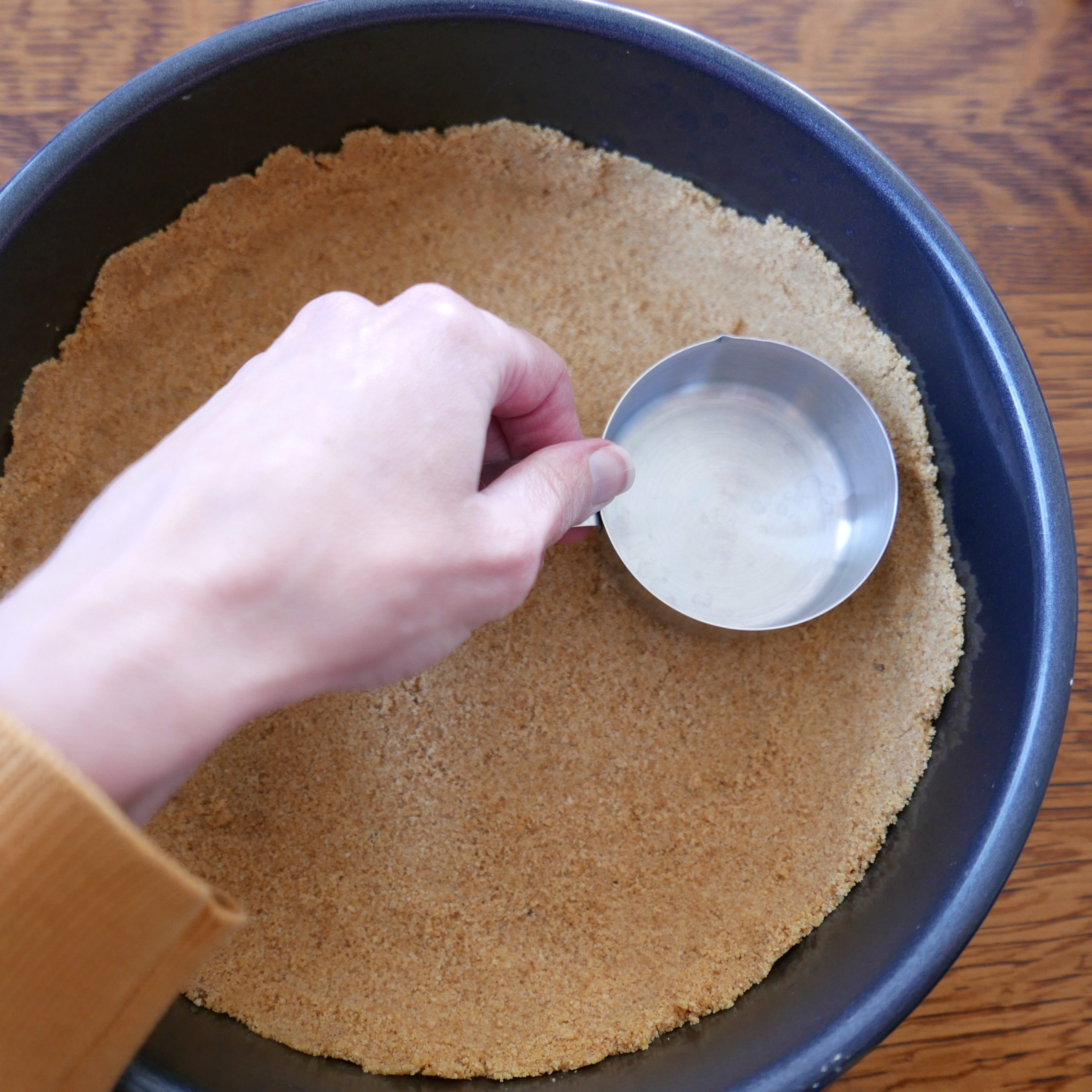 a white hand setting graham cracker crust into pie shell