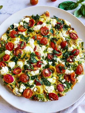 goat cheese frittata on a white platter with fresh basil.