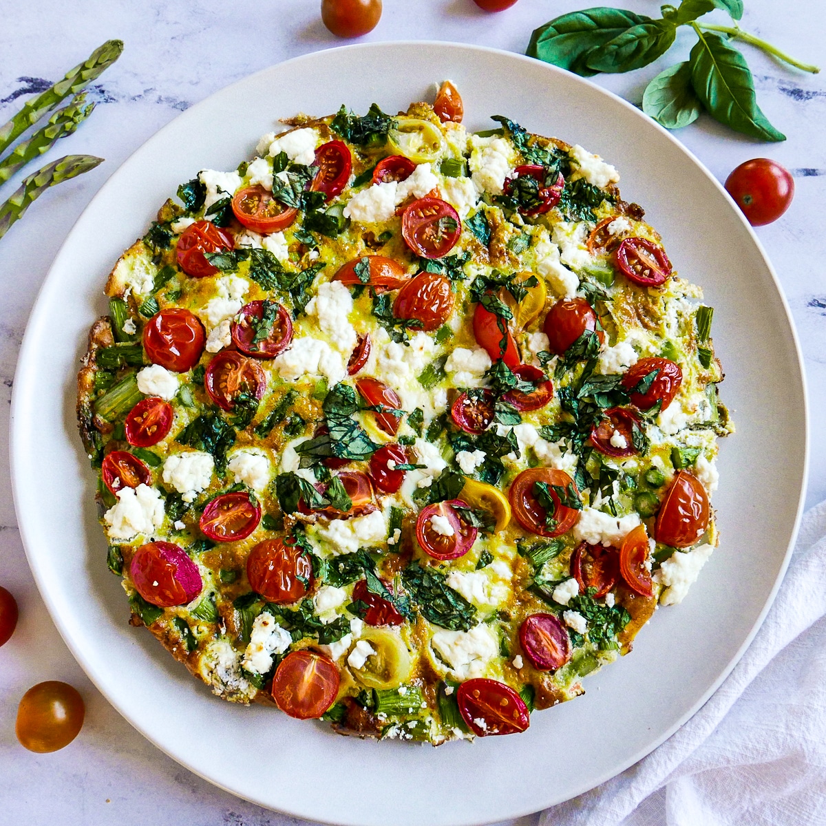 goat cheese frittata on a white platter with fresh basil.