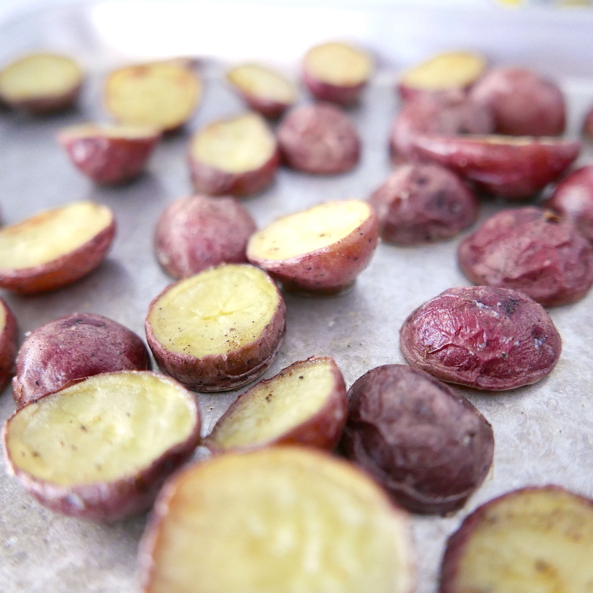 Roasted red potatoes spread out on a baking sheet.