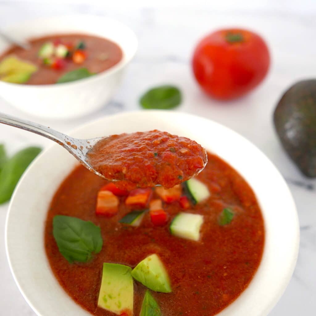silver spoon holding up a spoonful of gazpacho over a white bowl