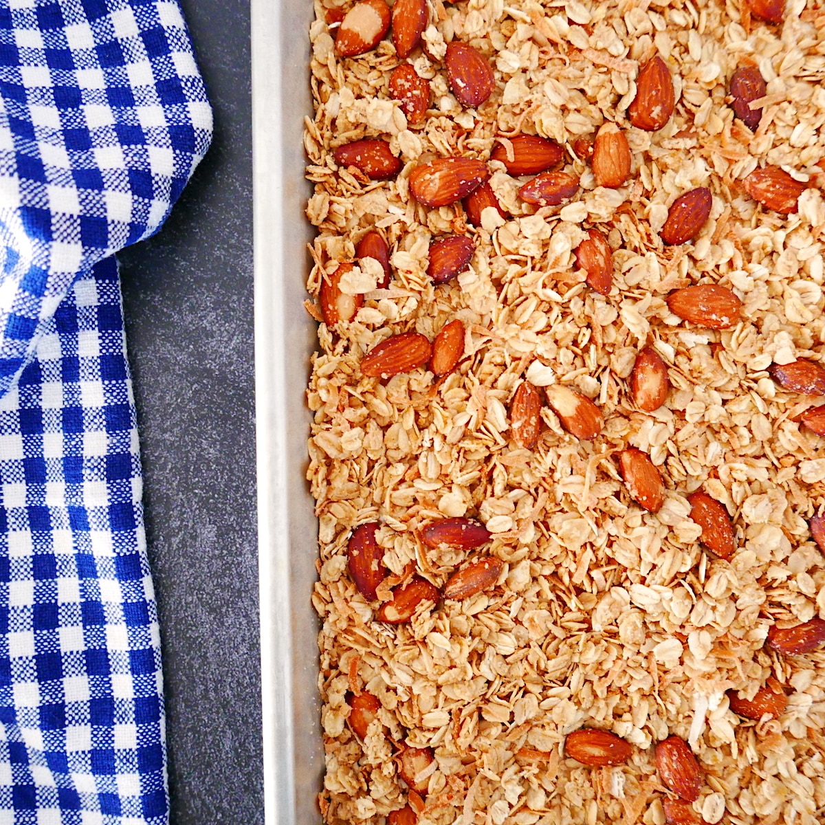 Pan of granola on a baking sheet with a checkered dish towel.