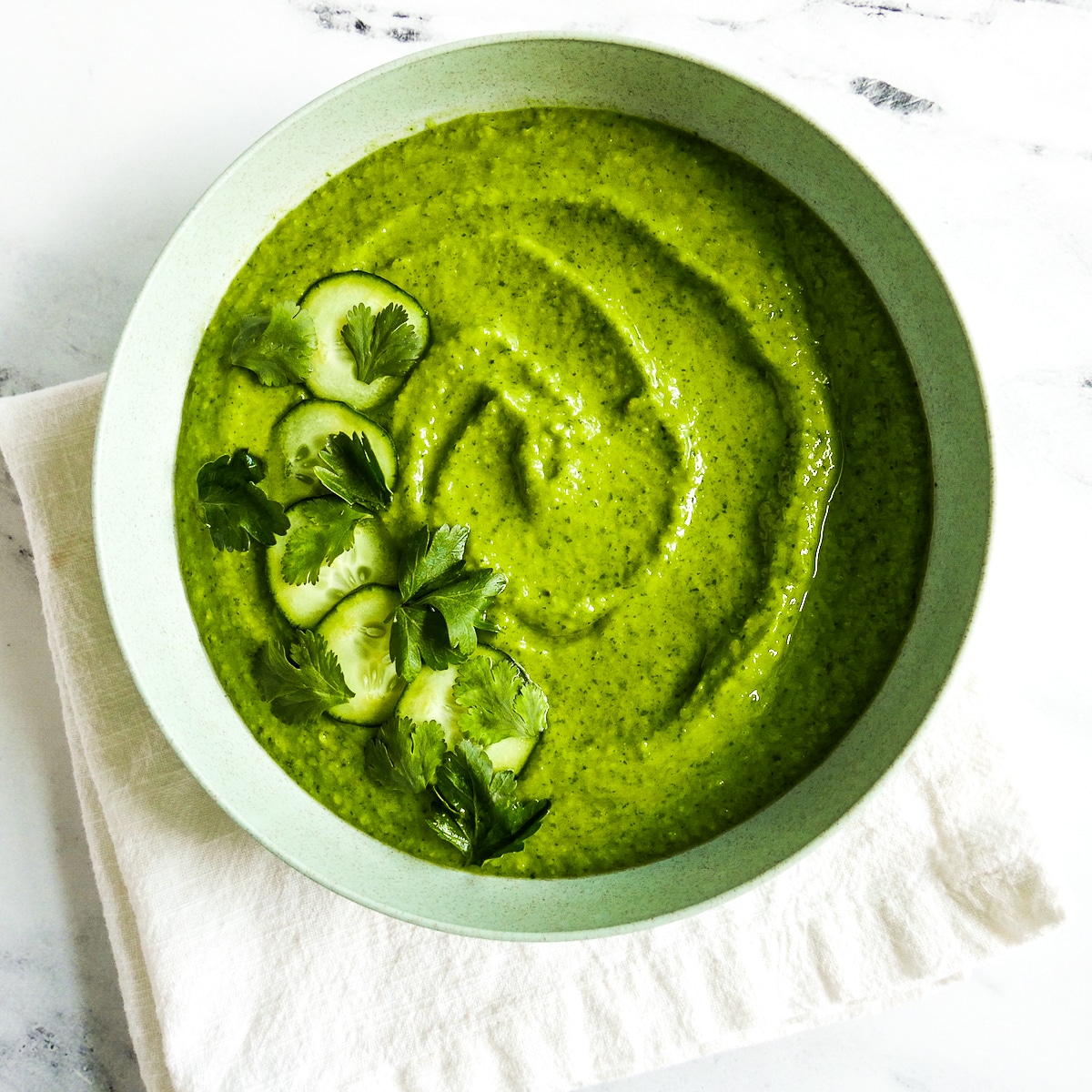 creamy avocado gazpacho in a white bowl resting on a white napkin.