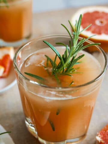 grapefruit vodka cocktail in a glass garnished with rosemary and slice of grapefruit.