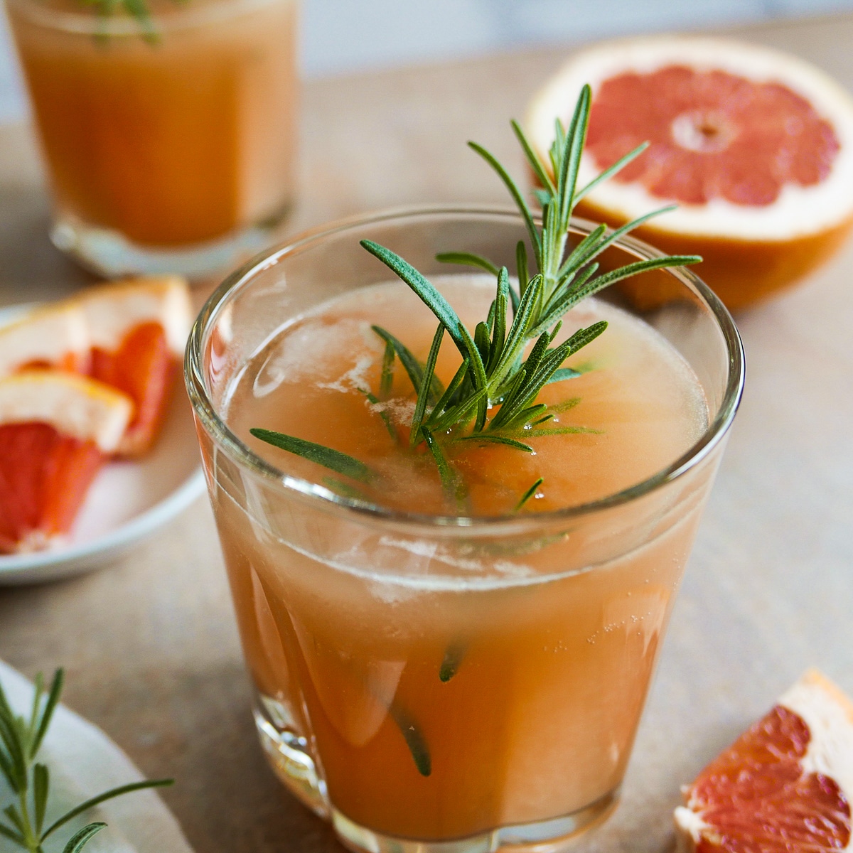 grapefruit cocktail in a glass garnished with rosemary and slice of grapefruit.