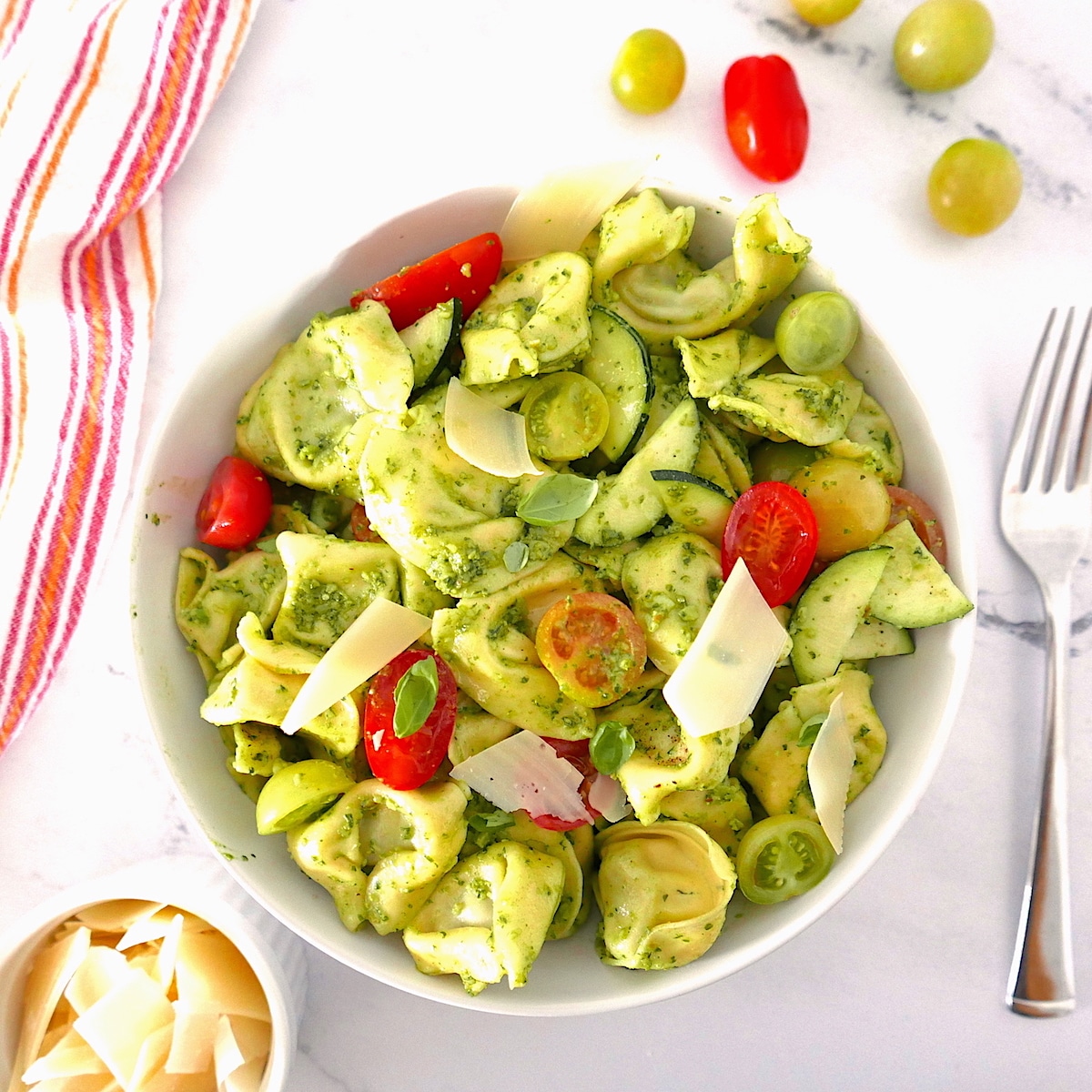 summer tortellini salad served in a white bowl on a marble counter with cherry tomatoes 