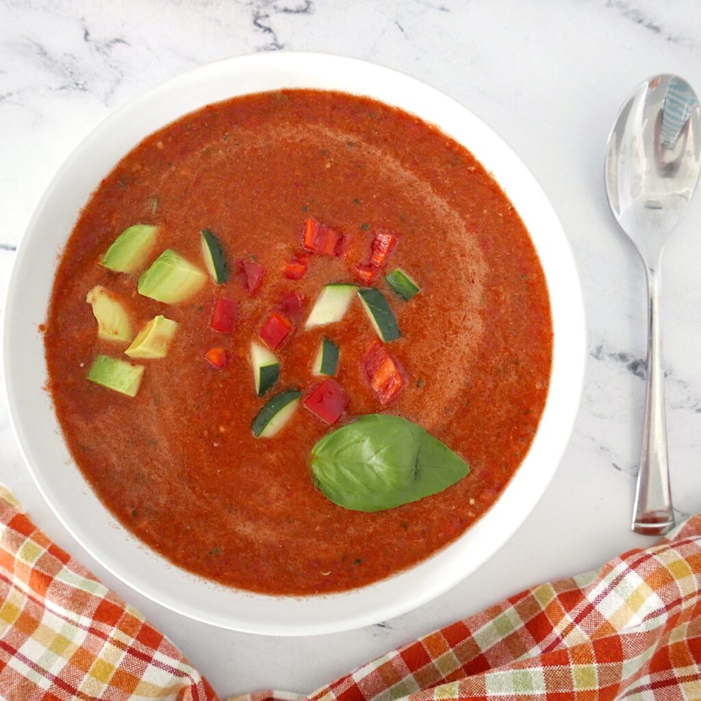 vegan cucumber gazpacho in a white bowl with avocado and basil on top