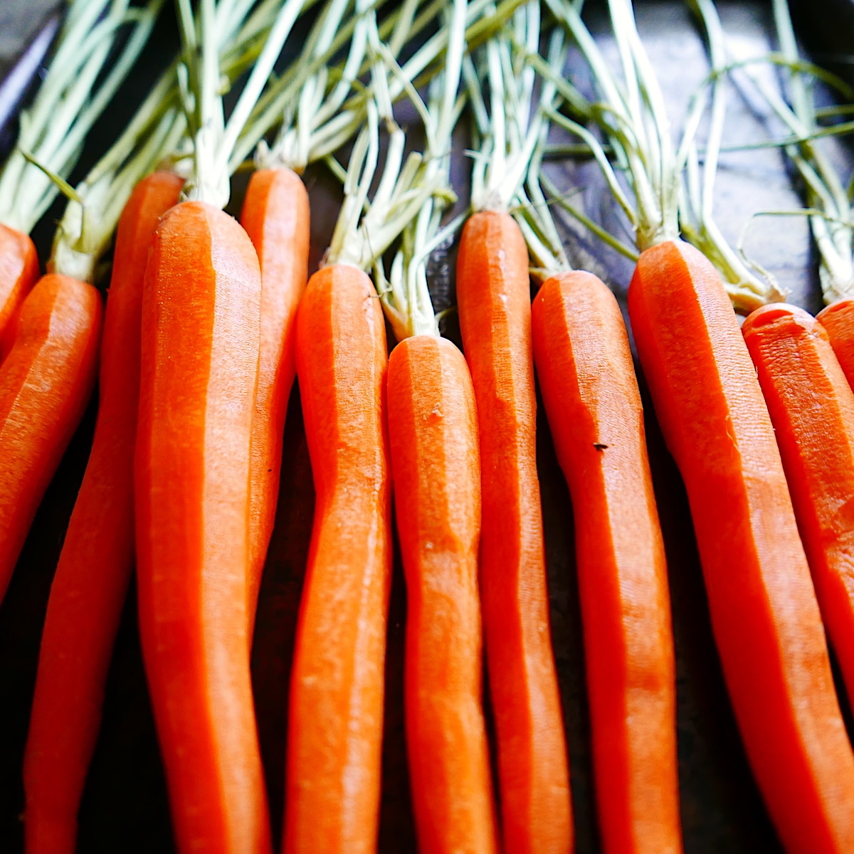 peeled carrots arranged on a baking sheet.