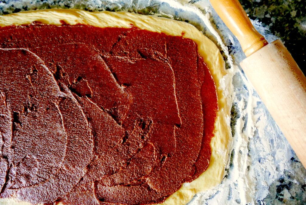 cinnamon buns being rolled out on a counter with flour and a rolling pin