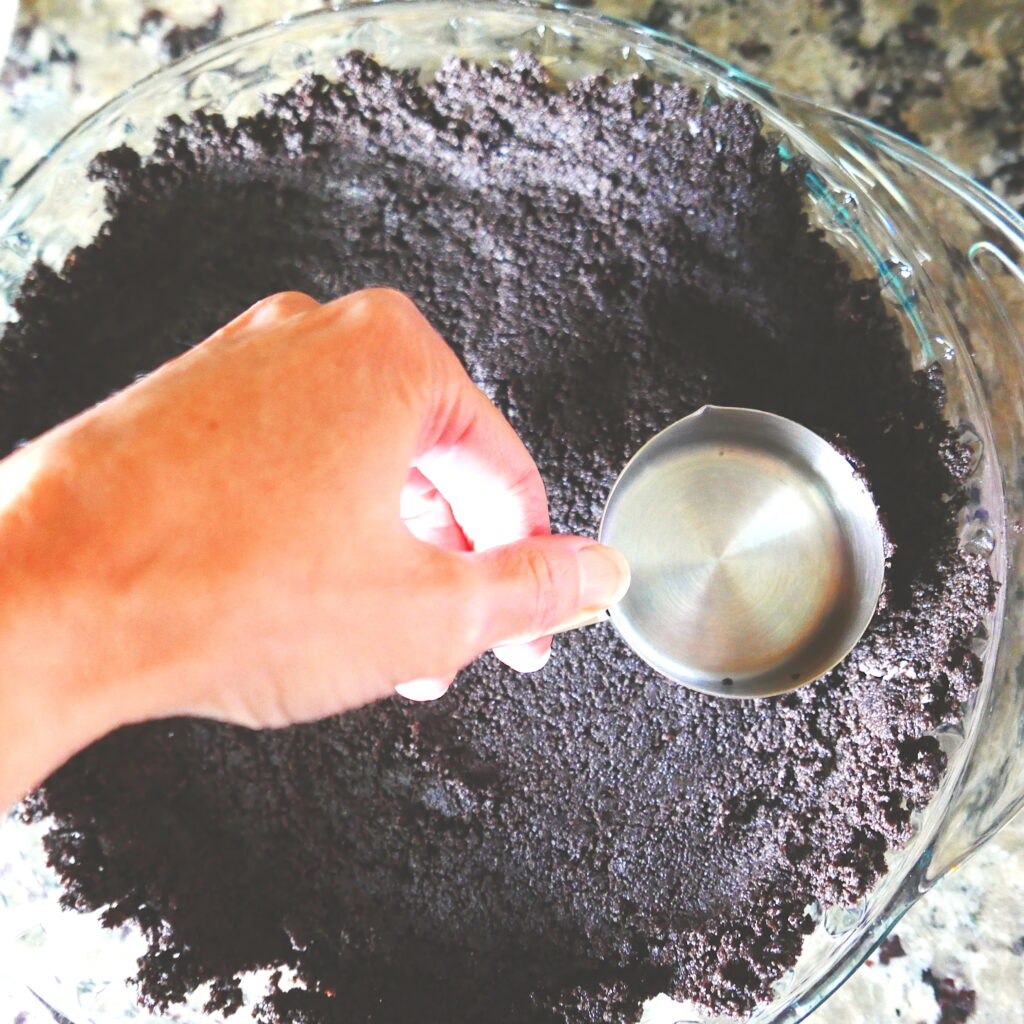 white hand pressing a measuring cup into chocolate pie crust