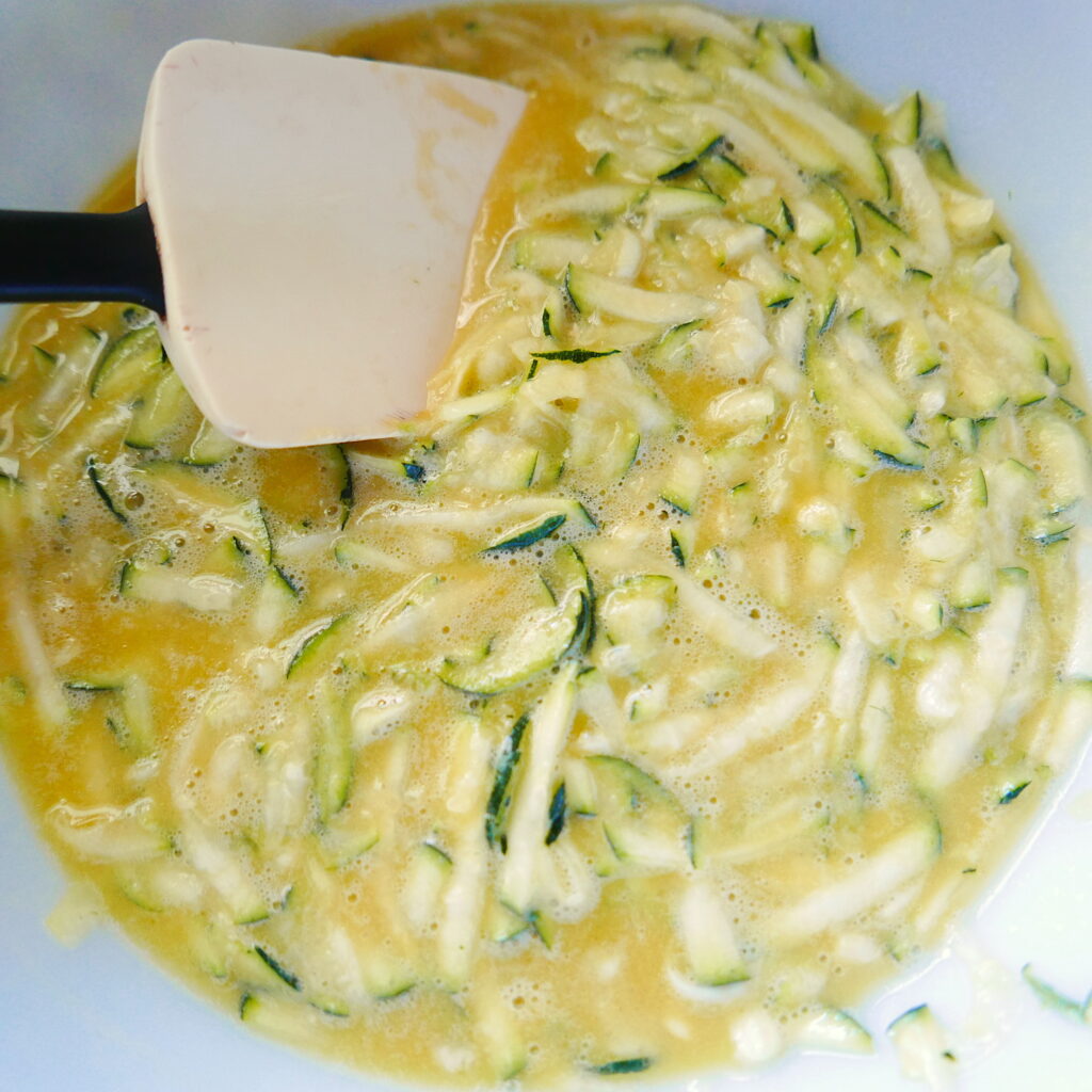 zucchini pancake batter being mixed together with a rubber spatula in a bowl