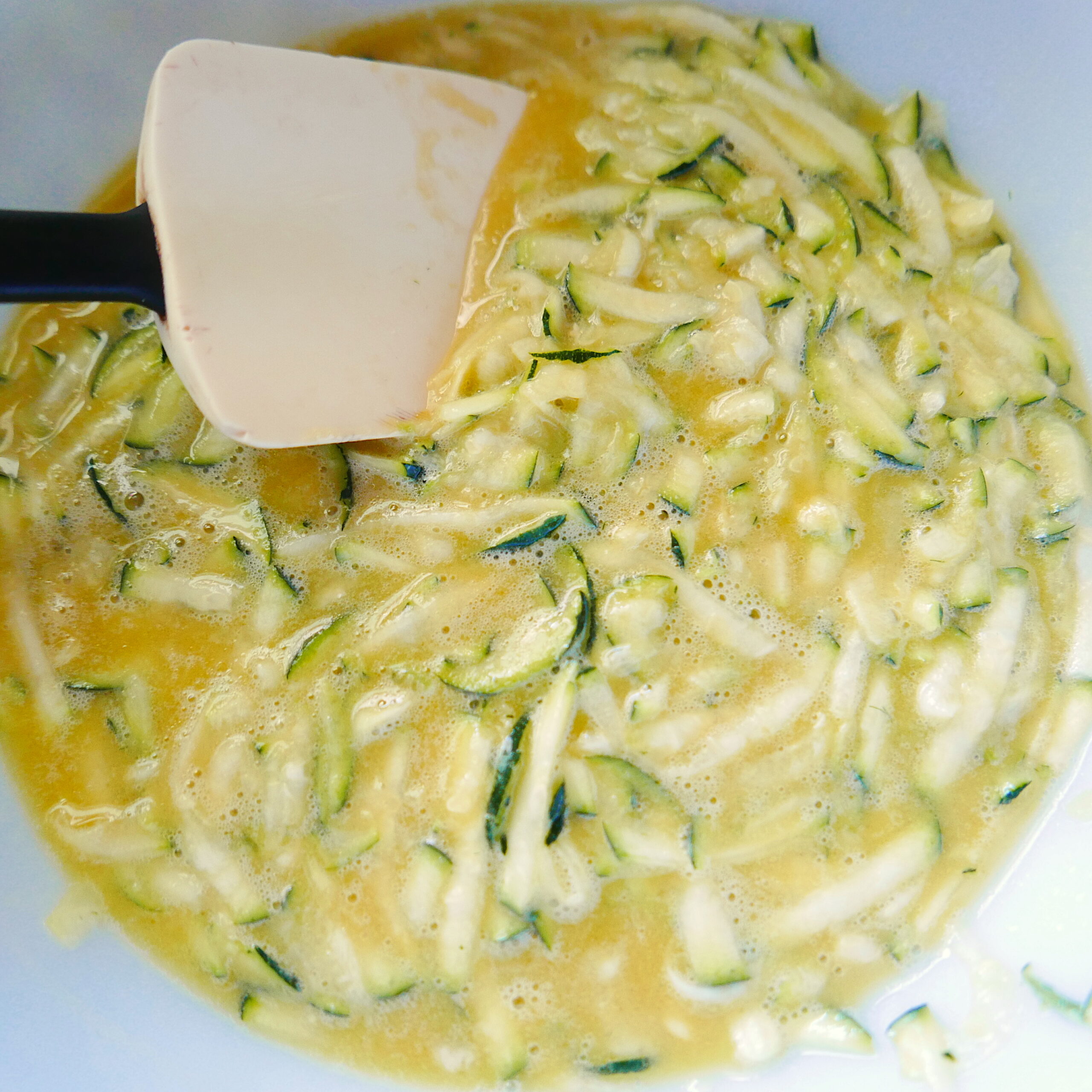 Eggs, olive oil, sugar, buttermilk, and vanilla extract being mixed together in a bowl.