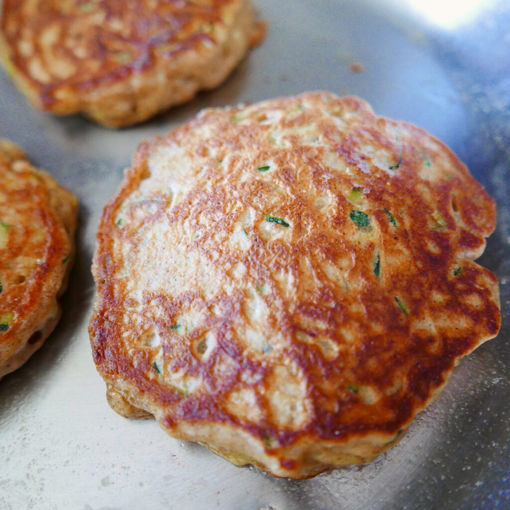 three zucchini bread pancakes in a skillet