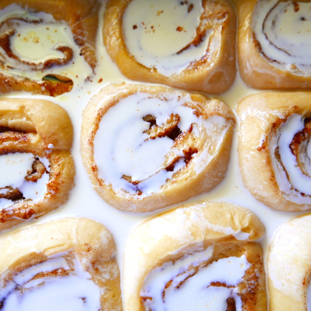 cinnamon buns covered in heavy cream in a baking dish