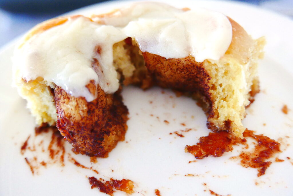 sticky and gooey cinnamon bun with cream cheese cut open and sitting on a white plate