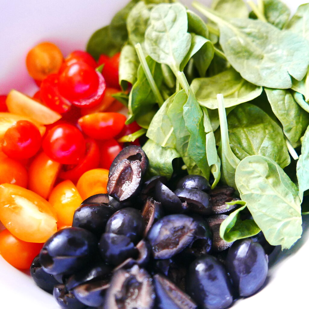 mixing bowl with spinach, black olives, and cherry tomatoes