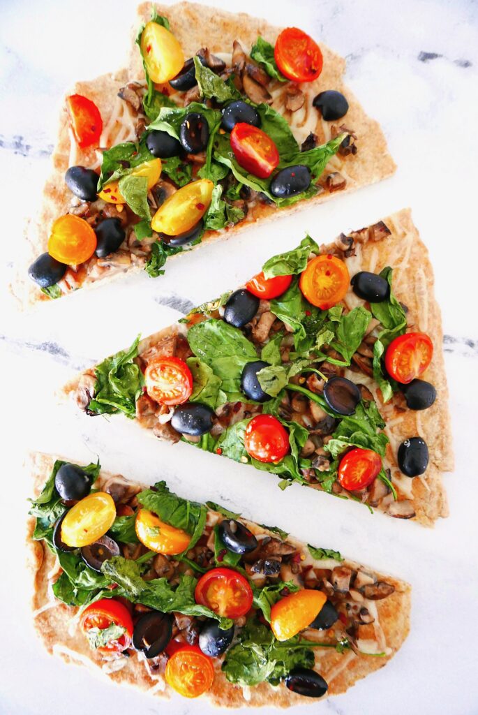 vegan flatbread pizza with lots of veggies cut into 3 slices and sitting on a marble counter